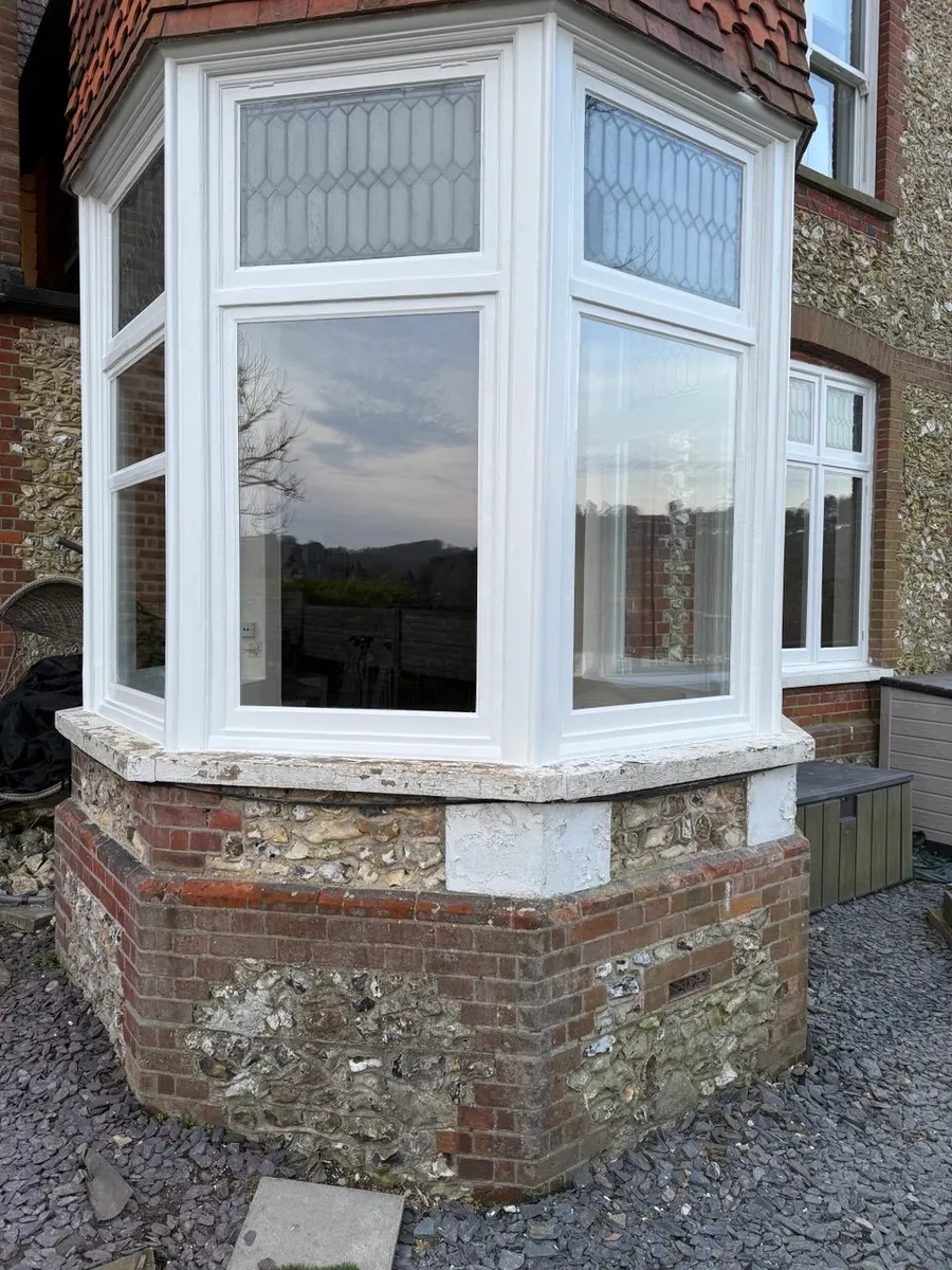 Restored white timber bay window with leaded upper lights on a flint and brick period house