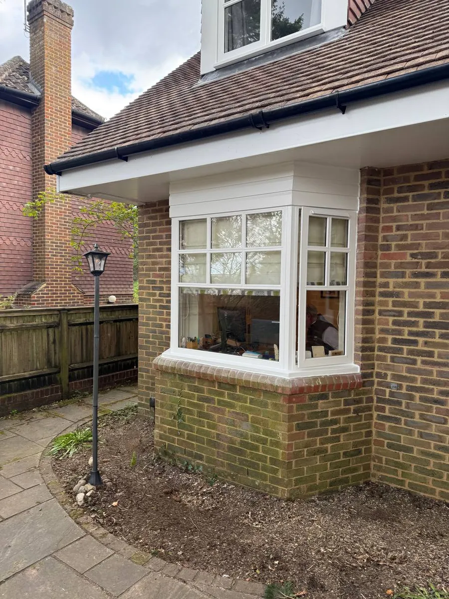 Restored white timber corner bay window with glazing bars on a brick house