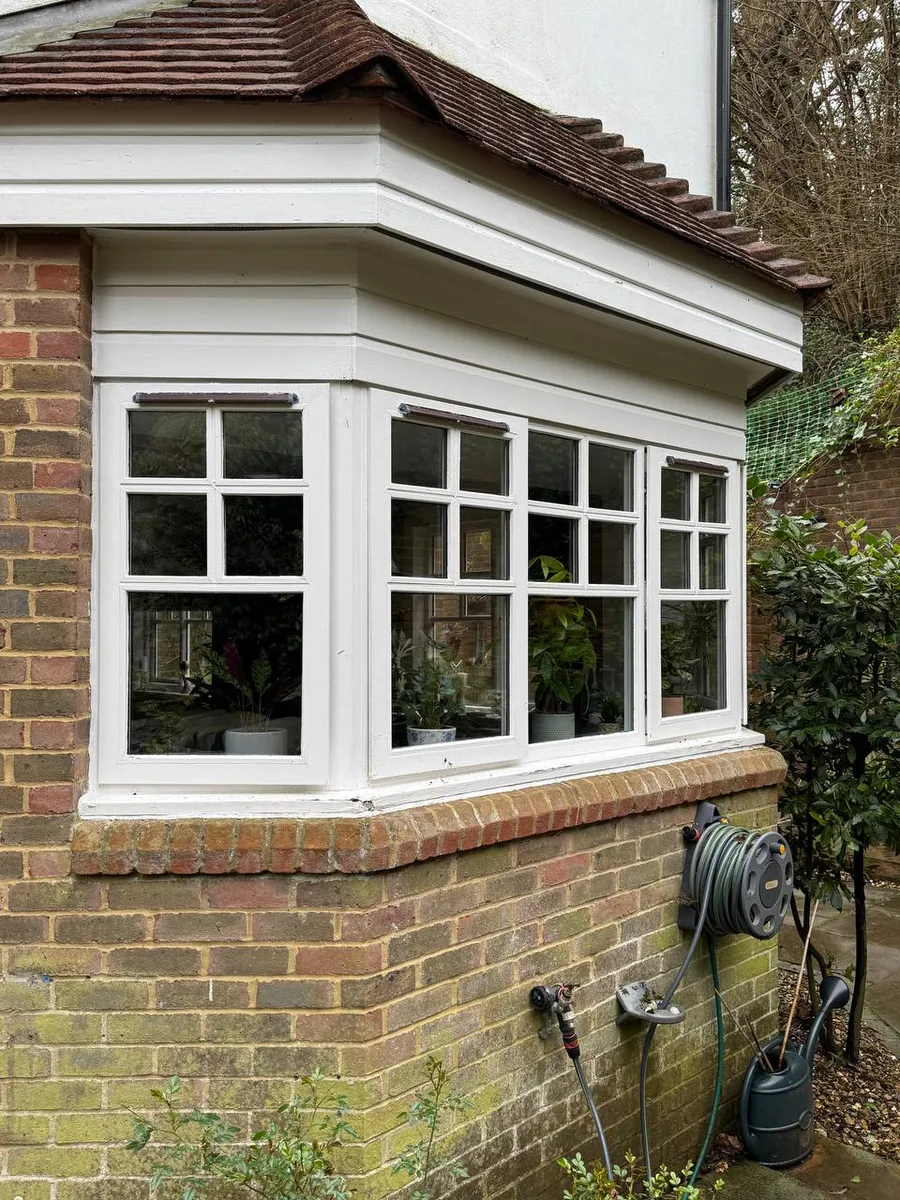 Restored white timber bay window with leaded panes on brick house corner