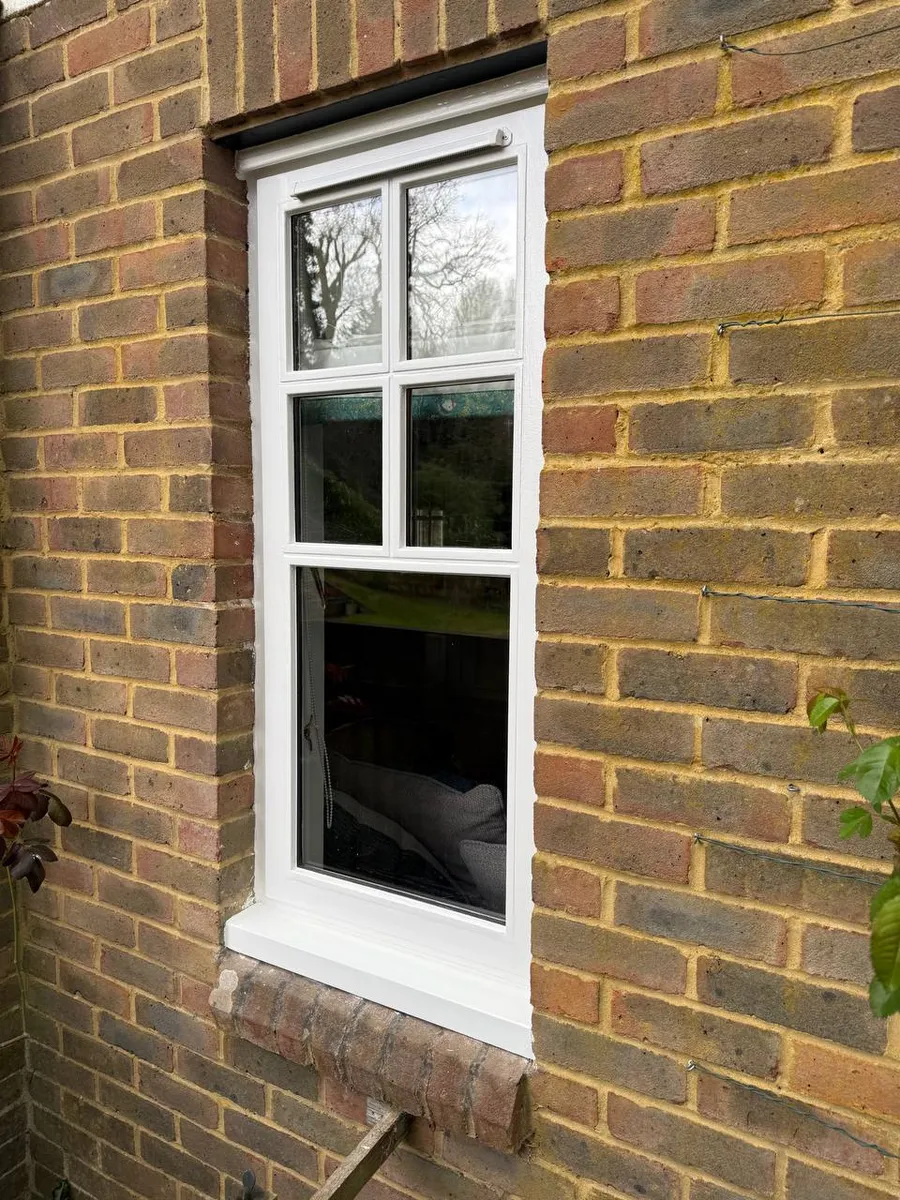 Restored white timber casement window with glazing bars set in a brick wall