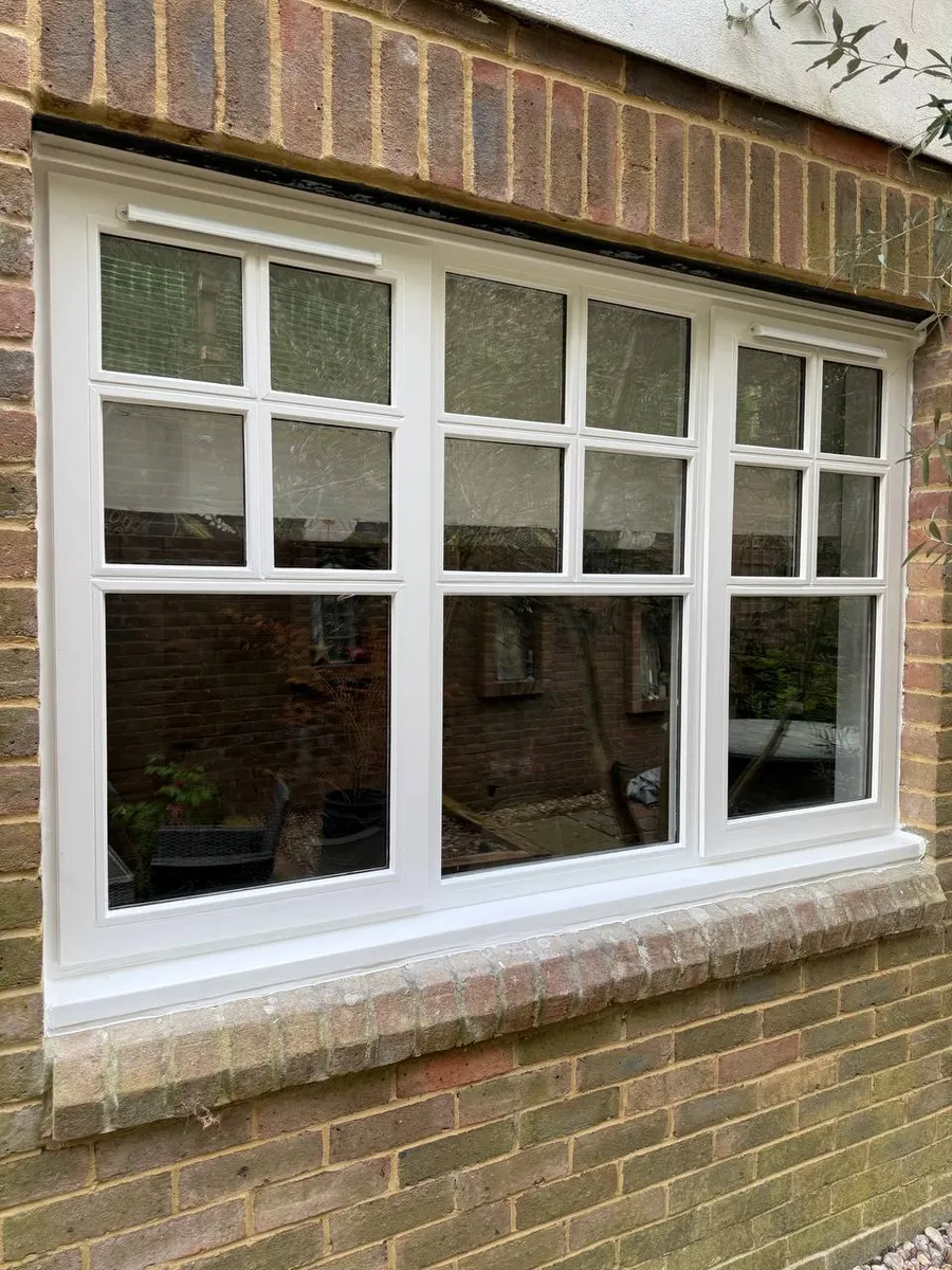 Restored white timber triple casement window with glazing bars in a brick wall