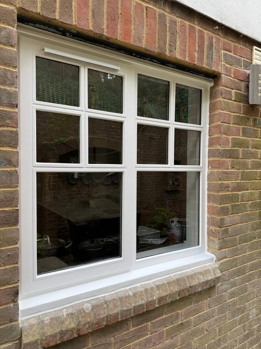 Restored white timber casement window with glazing bars set in a brick wall