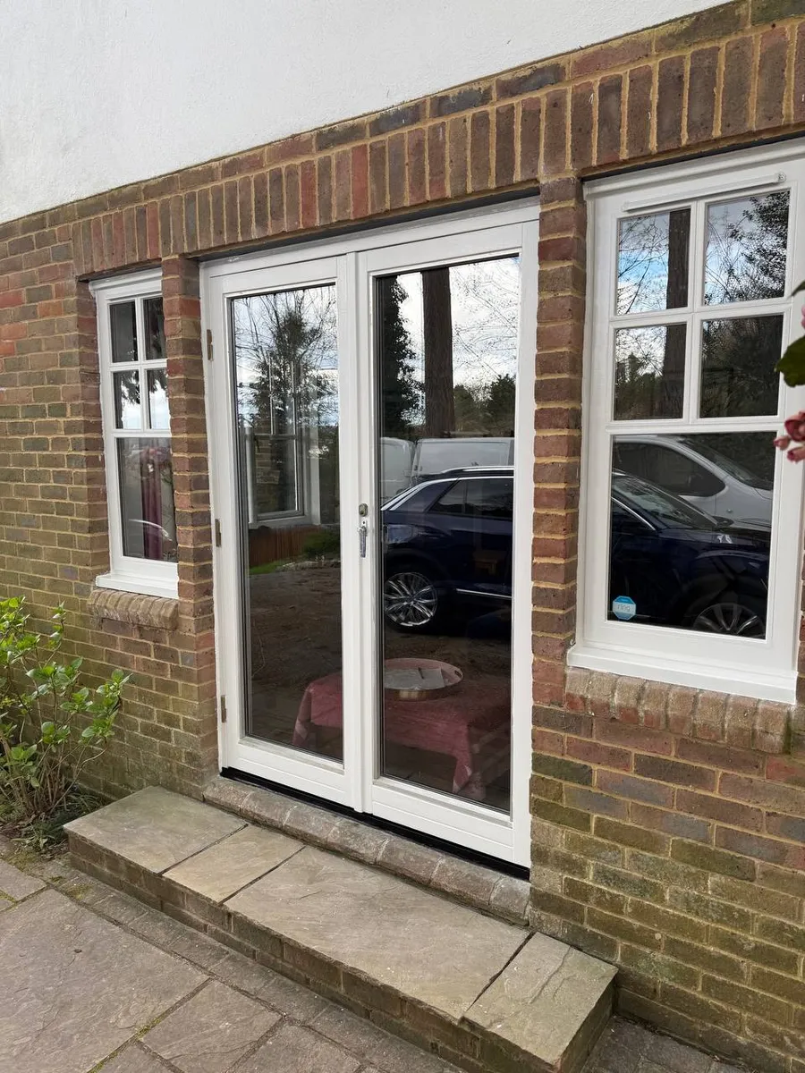 Restored white timber french doors with side casement windows on a brick house