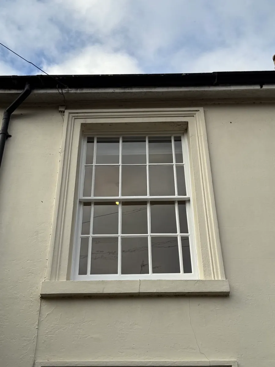 Restored white painted multi-pane timber sash window with bars in cream rendered period facade