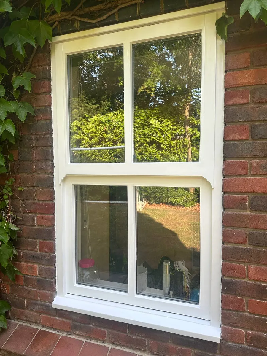 Restored cream timber sash window in a red-brick wall reflecting a garden hedge
